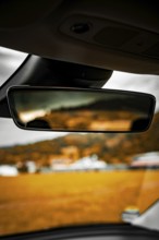 Rearview mirror in car with blurred view of landscape and buildings in background, Deer
