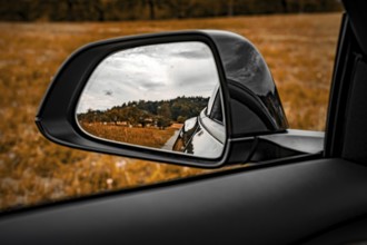 View through the side mirror of a car of a rural landscape with meadow and trees, Deer