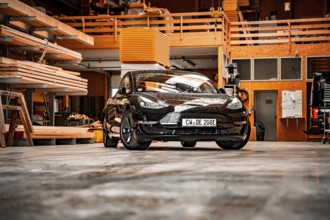 Black car parked in a workshop with wooden shelves and industrial atmosphere, Deer E-Carsharing,