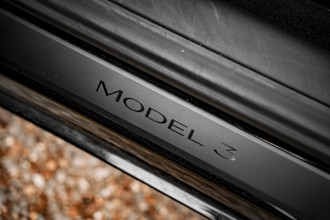 Close-up of a black car with model 3 emblem on a metallic surface, Deer E- car sharing, Tesla Model