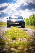 Black car on a sunny path surrounded by fields under a cloudy sky, Deer E- car sharing, Tesla Model