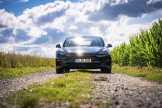 Front view of black car on rural road with cloudy sky, Deer E-Carsharing, Tesla Model 3, Calw,