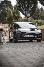 Black car from the front with surroundings and trees in the background, Deer e-Carsharing, Tesla