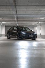 Black Tesla centrally positioned in empty, well-lit parking garage, Deer e-Carsharing, Tesla Model