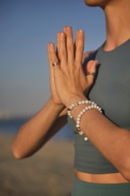 A woman practices yoga by holding hands in Namaskar Mudra at the beach as the sun sets in the