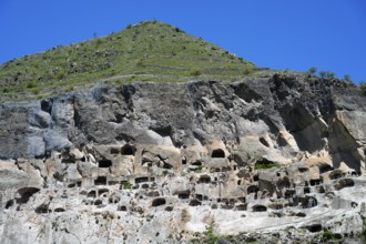 A steep mountain with numerous caves under a clear blue sky, cave town, cave monastery, Vardzia,