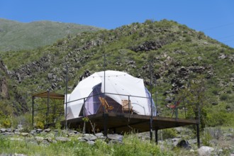 Dome tent on a wooden terrace in green mountain landscape under blue sky, Vardzia Glamping,