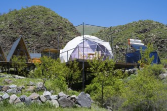 A modern dome tent in a mountainous landscape under blue sky, surrounded by green nature, Vardzia