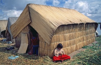 Little girl sitting in front of a reed hut on a floating Uro island in Lake Titcaca, Peru, South
