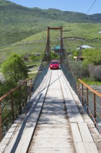 A car drives across a wooden suspension bridge in green surroundings, Kura River near Nijgori,