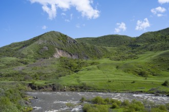 Green hills and a river under a blue sky offer a peaceful landscape, Kura River between