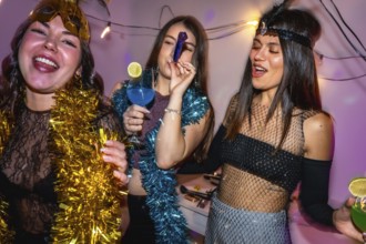 Young women in vibrant costumes laugh and clink cocktails at a festive new year's eve party