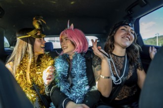 Three young women wearing festive costumes and tinsel garlands, smiling and laughing together while