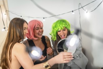 Two young women in pink and green wigs laugh and celebrate at a colorful house party, sharing