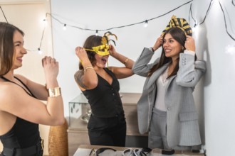 Happy young women enjoying a costume party at home, laughing and having fun while trying on masks