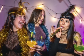 Three diverse young women in festive costumes laughing and toasting with colorful cocktails and