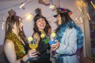Three diverse young women friends wearing festive costumes and tinsel, celebrating a new year's eve