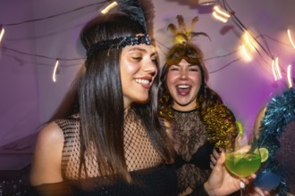 Joyful women wearing festive costumes and headbands, holding cocktails and laughing, enjoying a fun