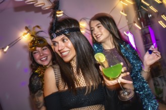 Three friends smiling and celebrating a festive costume party at home, holding a green cocktail and