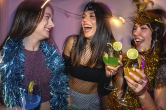 Group of women laughing and holding cocktails while celebrating with party decorations, enjoying a
