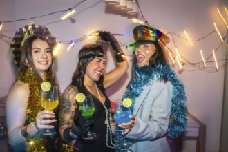 Three diverse women wearing festive costumes, decorations, and holding colorful cocktails, enjoying