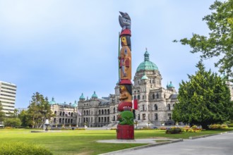 Totem pole standing tall with parliament buildings in the background, showcasing the blend of