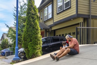 Father and son enjoying quality time together, sitting on their driveway on a sunny summer day,