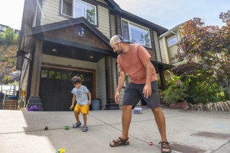 Father and son are bending down and playing with toy cars on the driveway of their house in canada