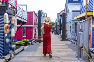 Tourist wearing a straw hat and a red jumpsuit is walking on a wooden boardwalk between colorful