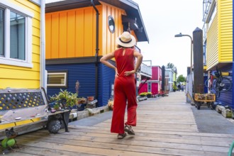 Young woman tourist in a straw hat and red jumpsuit walking along a wooden boardwalk, admiring