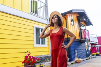 Happy female tourist wearing a straw hat and red dress is posing and smiling in front of the