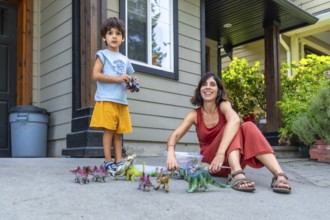 Happy mother and son enjoying quality time together, playing with dinosaur toys on their porch in