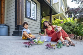 Mother and son sitting on the ground in their front yard, enjoying a sunny summer day while playing