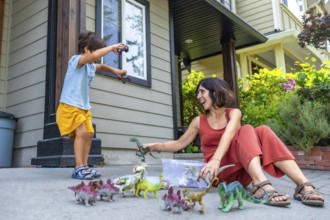 Happy mother and son enjoying quality time together, playing with dinosaur toys outside their house