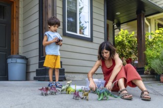 Mother and son enjoying quality time together, playing with dinosaur toys on the porch of their