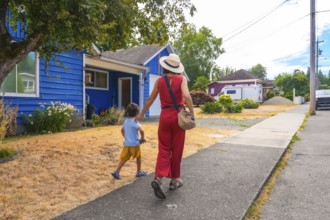 Mother and son walking away from a colorful blue house on a summer day in a residential