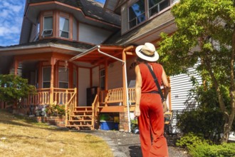 Tourist wearing a straw hat and a red jumpsuit is walking on a path near a traditional wooden house