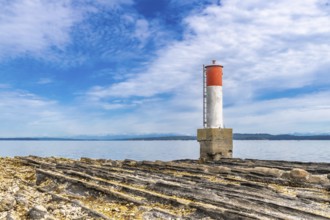 Red and white navigation marker stands on a rocky coastline in chemainus, british columbia, with