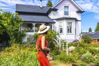 Tourist wearing a straw hat and orange dress walking through a colorful blooming garden in front of