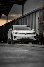 White car between freight cars at dusk, VW ID4 electric car, Deer Carsharing, Calw, Germany