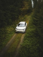 A white Volkswagen drives along a green forest path, VW ID4 electric car, Deer Carsharing, Calw,