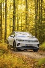 An SUV drives on a forest path in autumn surrounded by yellow leaves under bright sunlight, VW ID4