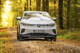 White car on an autumnal forest road, VW ID4 electric car, Deer Carsharing, Calw, Germany