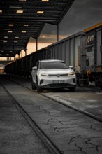 White car at night next to freight trains in depot, VW ID4 electric car, Deer Carsharing, Calw,