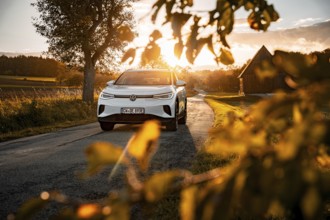 White car at sunset on the road with a farm in the background, VW ID4 electric car, Deer