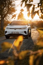 White car on a country road at sunset surrounded by leaves, VW ID4 electric car, Deer Carsharing,