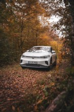 A white Volkswagen in the woods with warm autumn leaves, VW ID4 electric car, Deer Carsharing,
