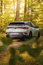 White car in autumn forest with yellow leaves on the ground, VW ID4 electric car, Deer Carsharing,