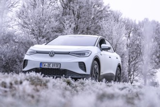 A white car is parked in a frosty winter landscape with snow-covered trees, VW ID4 electric car,