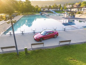 Red sports car at the edge of a swimming pool in a park during daylight, Porsche Taycan, Deer